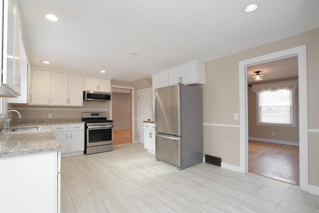 kitchen featuring light stone counters, recessed lighting, appliances with stainless steel finishes, white cabinetry, and a sink