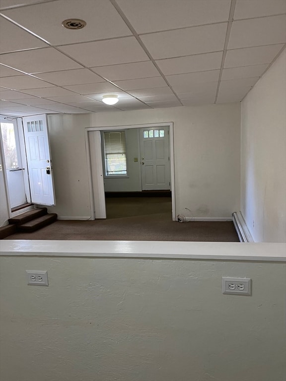 foyer featuring dark colored carpet, baseboard heating, a drop ceiling, and a healthy amount of sunlight