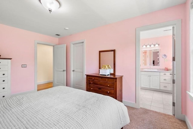 bedroom featuring light colored carpet, baseboards, a sink, ensuite bath, and visible vents