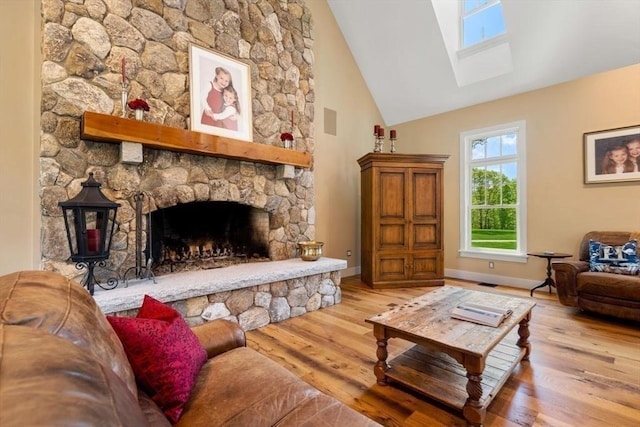 living room with high vaulted ceiling, a skylight, baseboards, a fireplace, and wood finished floors