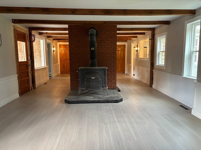 unfurnished living room featuring beamed ceiling, light hardwood / wood-style flooring, and a wood stove