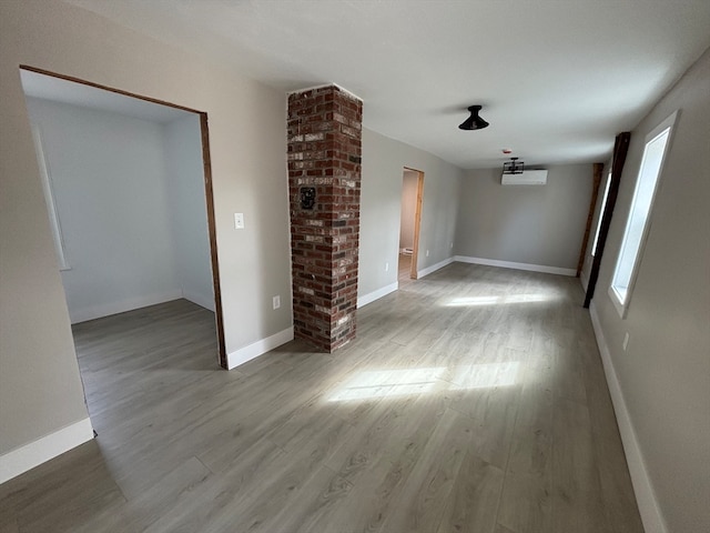 unfurnished living room featuring decorative columns and light wood-type flooring