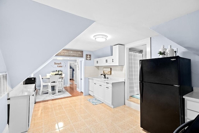 kitchen featuring freestanding refrigerator, a sink, white cabinetry, and light countertops