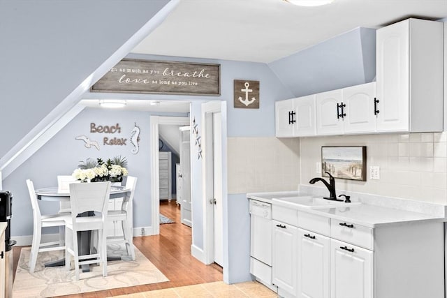 kitchen with dishwasher, a sink, light countertops, lofted ceiling, and white cabinetry