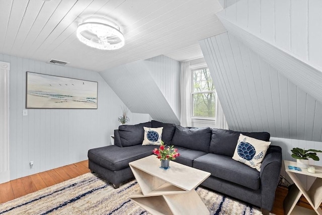 living area featuring visible vents, wood walls, lofted ceiling, and wood finished floors