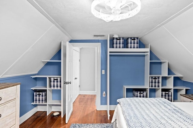 bedroom featuring visible vents, wood-type flooring, baseboards, a textured ceiling, and vaulted ceiling