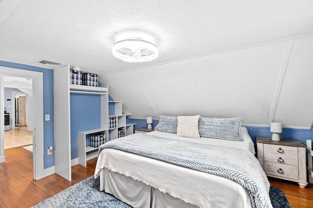 bedroom with baseboards, lofted ceiling, wood finished floors, and visible vents