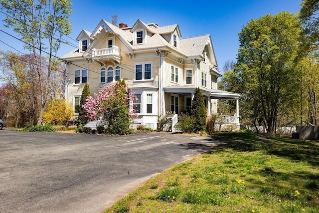 view of front of house featuring a front yard, a balcony, covered porch, and a chimney
