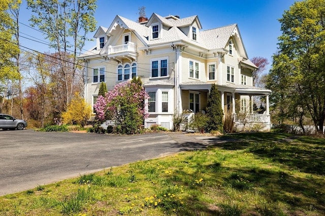 victorian house with a front yard, covered porch, and a chimney
