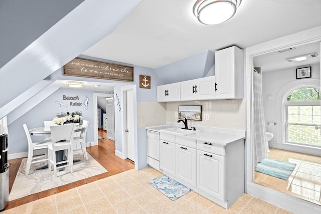 kitchen with white dishwasher, a sink, light countertops, white cabinets, and lofted ceiling