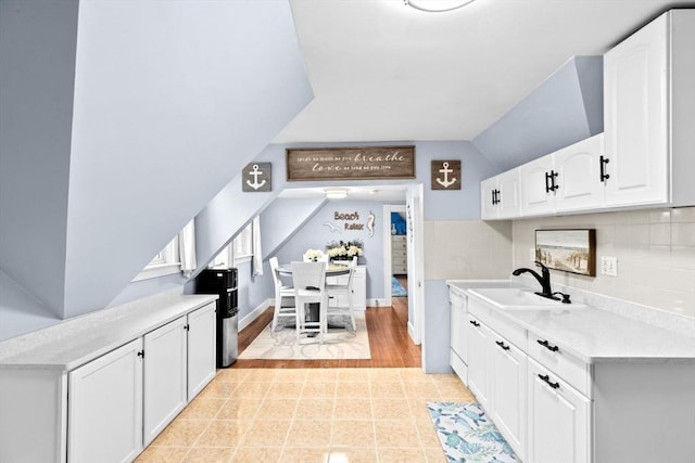 kitchen featuring light countertops, white cabinets, a sink, backsplash, and vaulted ceiling