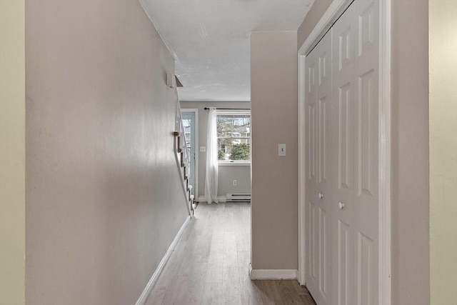 corridor with stairs, a baseboard radiator, light wood-style flooring, and baseboards