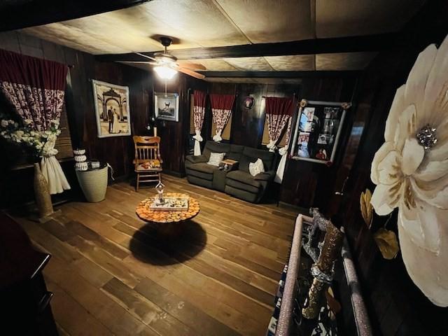 living room with wooden walls, beamed ceiling, ceiling fan, and wood finished floors