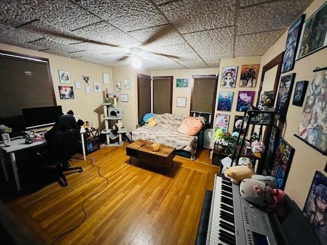 interior space with a paneled ceiling, a ceiling fan, and wood finished floors