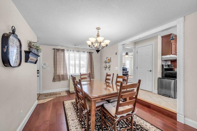 dining room with baseboards, a textured ceiling, light wood finished floors, and ceiling fan with notable chandelier