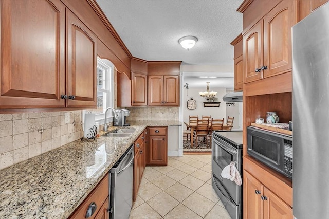 kitchen with brown cabinetry, wall chimney exhaust hood, appliances with stainless steel finishes, light stone countertops, and a sink