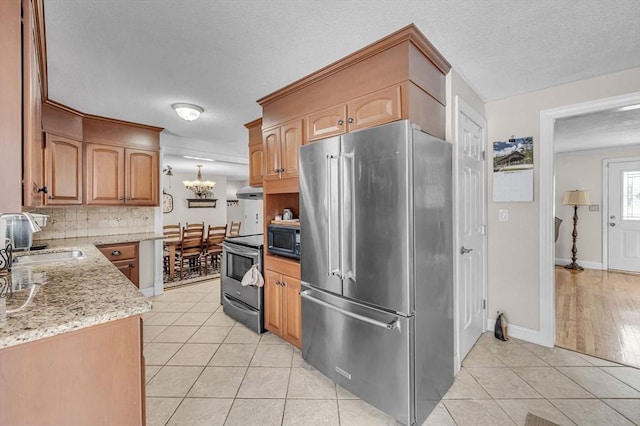 kitchen with light tile patterned floors, stainless steel appliances, decorative backsplash, an inviting chandelier, and a sink