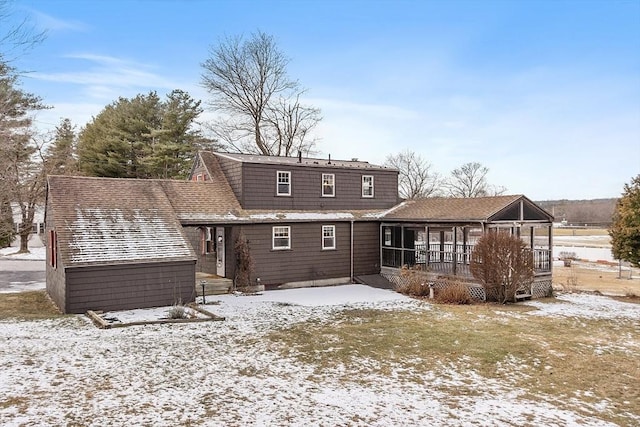 snow covered rear of property with a sunroom