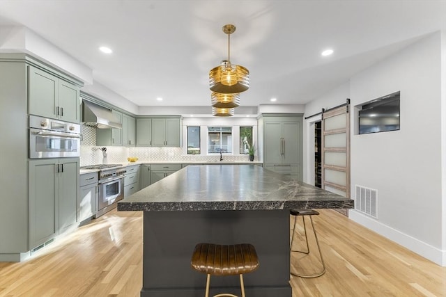 34 Walker St, Somerville, MA 02144 - kitchen featuring green cabinets, wall chimney range hood, stainless steel appliances, a barn door, and light wood-type flooring
