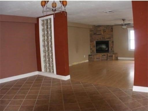 unfurnished living room featuring ceiling fan with notable chandelier, dark wood-type flooring, and a fireplace