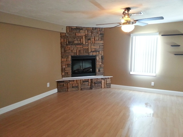 unfurnished living room featuring a stone fireplace, hardwood / wood-style floors, and ceiling fan