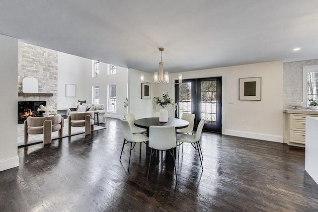 dining room with dark wood finished floors, a fireplace, baseboards, and an inviting chandelier