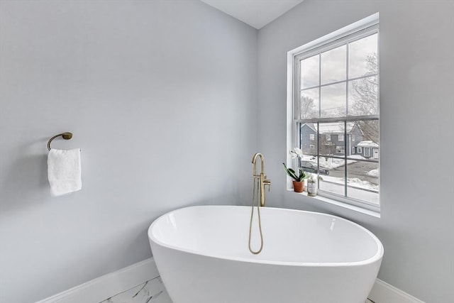 bathroom with a soaking tub, baseboards, and marble finish floor