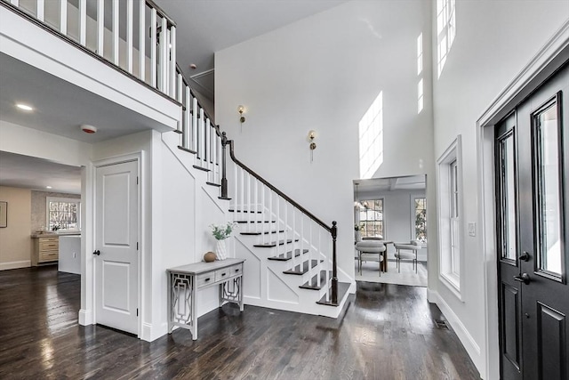 foyer with a healthy amount of sunlight, dark wood-style floors, stairs, and a towering ceiling