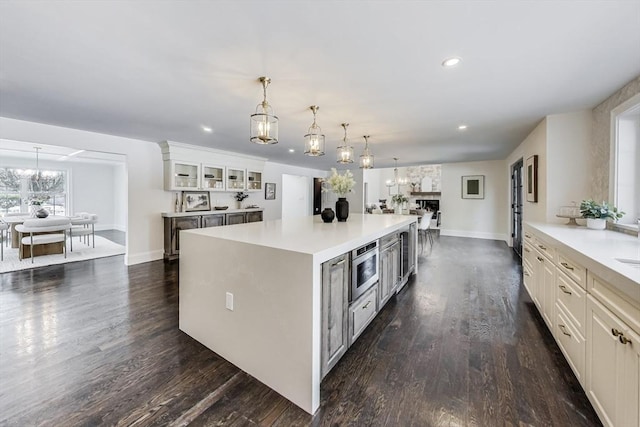 kitchen featuring decorative light fixtures, a kitchen island, open floor plan, light countertops, and glass insert cabinets