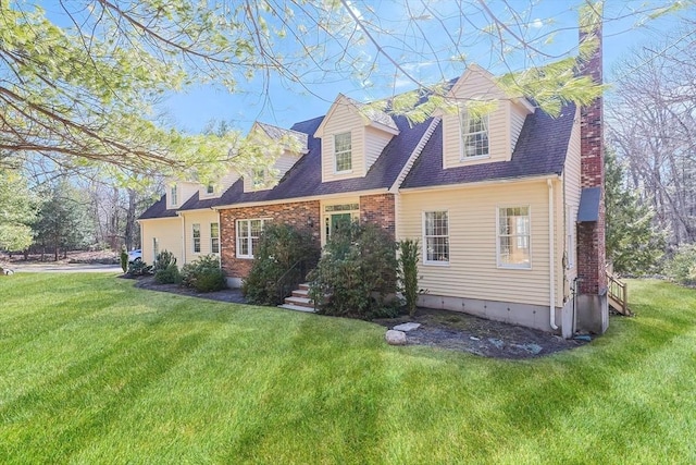 cape cod house with brick siding, a front yard, roof with shingles, and a chimney