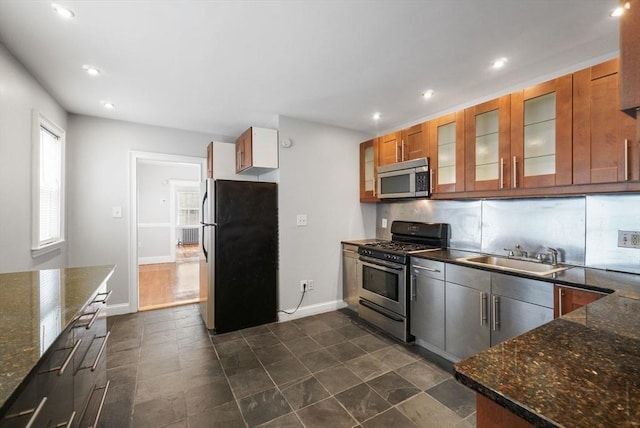 kitchen featuring tasteful backsplash, glass insert cabinets, appliances with stainless steel finishes, brown cabinetry, and a sink