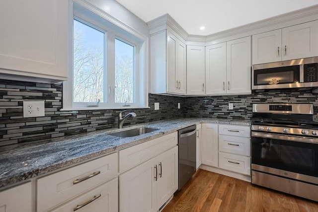 kitchen featuring light stone counters, wood finished floors, stainless steel appliances, white cabinetry, and a sink