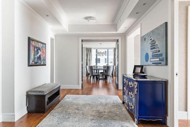 hallway with a raised ceiling, wood finished floors, a chandelier, baseboards, and ornamental molding