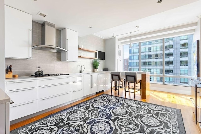kitchen with wall chimney exhaust hood, gas cooktop, modern cabinets, backsplash, and open shelves