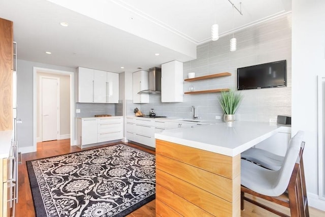 kitchen with wall chimney exhaust hood, a peninsula, decorative backsplash, a sink, and white cabinetry