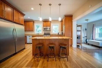 kitchen featuring pendant lighting, stainless steel appliances, brown cabinetry, and a kitchen breakfast bar