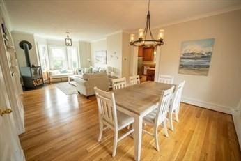 dining area with a wood stove, baseboards, ornamental molding, and wood finished floors