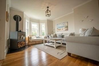 living room featuring a wood stove, crown molding, and wood finished floors