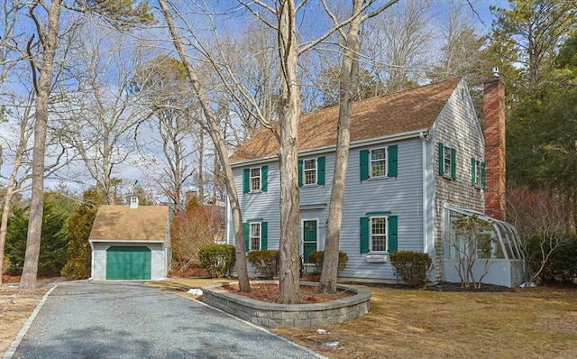 colonial house featuring a garage, roof with shingles, an outdoor structure, and a chimney