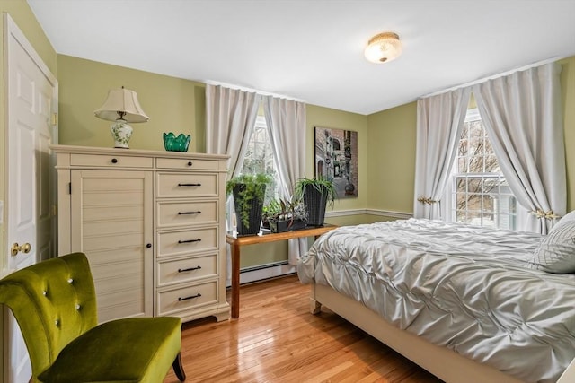 bedroom featuring a baseboard heating unit, multiple windows, and light wood finished floors