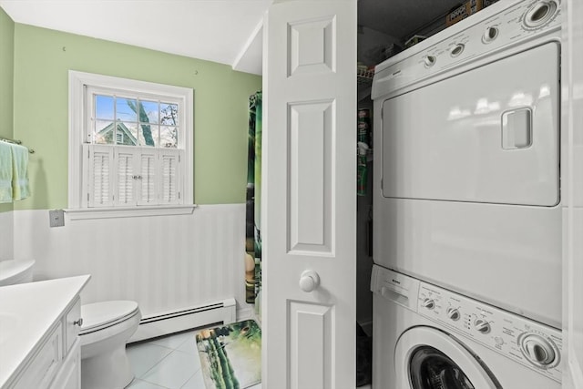 laundry area with a baseboard heating unit, stacked washer / drying machine, and light tile patterned floors