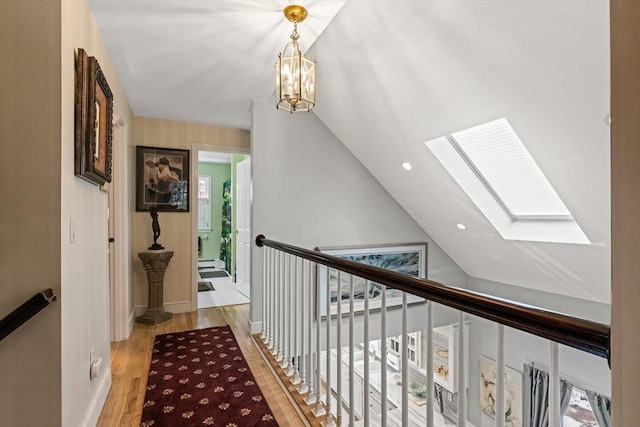 hall with a notable chandelier, an upstairs landing, baseboards, light wood-style floors, and lofted ceiling with skylight