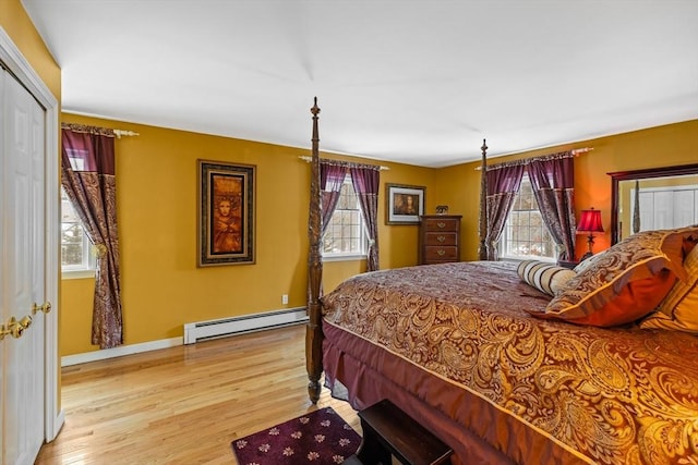 bedroom with a baseboard heating unit, multiple windows, light wood-style flooring, and baseboards