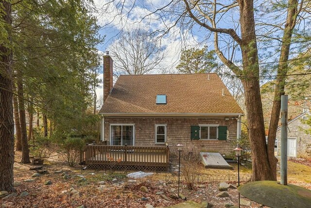 back of house with a chimney, a deck, and roof with shingles