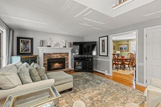 living room with a brick fireplace, a baseboard radiator, baseboards, and wood finished floors