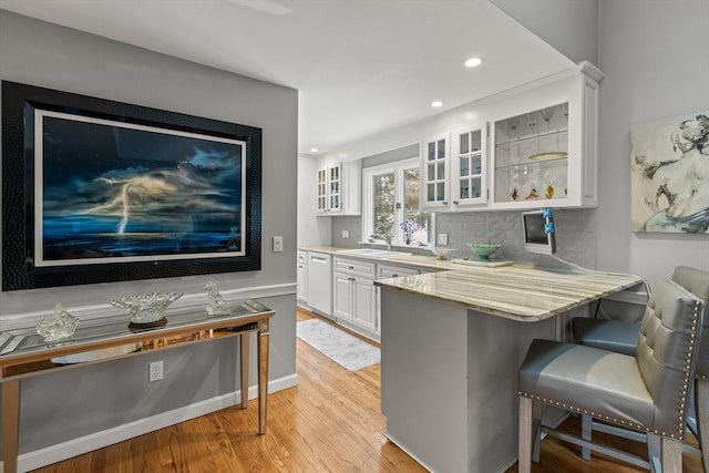 kitchen featuring white cabinets, glass insert cabinets, a breakfast bar area, a peninsula, and light stone countertops