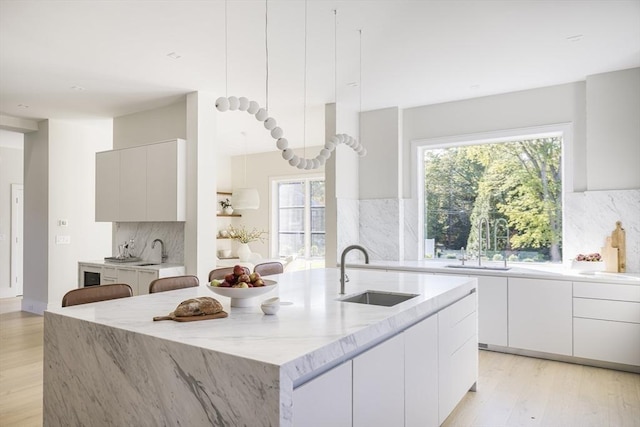 kitchen featuring sink, white cabinets, a kitchen island with sink, and decorative backsplash