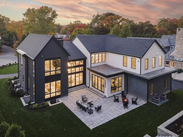 back house at dusk with a fire pit, a patio area, a yard, and cooling unit