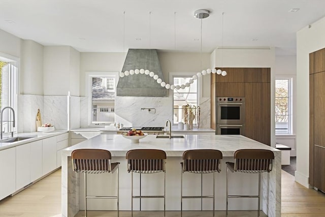 kitchen featuring sink, white cabinetry, tasteful backsplash, a kitchen island with sink, and stainless steel double oven