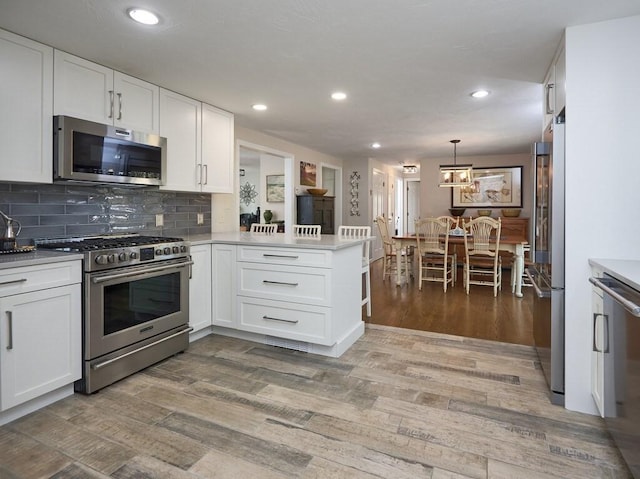 kitchen featuring light wood-type flooring, appliances with stainless steel finishes, a peninsula, and white cabinetry